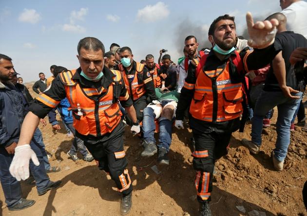 Des Palestiniens transportent un homme blessé lors d'affrontements avec les forces israéliennes près de la frontière entre la bande de Gaza et Israël le 27 avril 2018 [MOHAMMED ABED / AFP]
