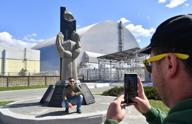 Des touristes se photographient devant la la nouvelle chape recouvrant le 4e réacteur accidenté de la centrale de Tchernobyl le 23 avril 2018 [Sergei SUPINSKY / AFP]