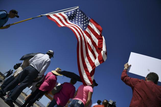 Des manifestants déploient le drapeau américain lors d'un rassemblement près d'un poste-frontière avec le Mexique, au Texas, pour protester contre les séparations de familles de migrants, le 21 juin 2018  [Brendan Smialowski / AFP]