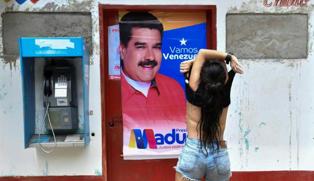 Une femme soulève son tee-shirt devant une affiche de campagne du président vénézuélien, Nicolas Maduro, dans l'Etat de Choroni-Aragua, au Vénézuela, le 12 mai 2018 [JUAN BARRETO / AFP]