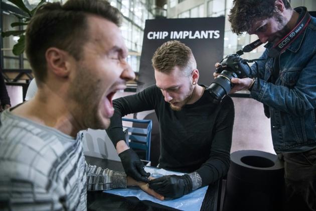 Un homme réagit alors qu'un autre insère un implant sous sa peau, à Stockholm, le 18 janvier 2018 [Jonathan NACKSTRAND / AFP]