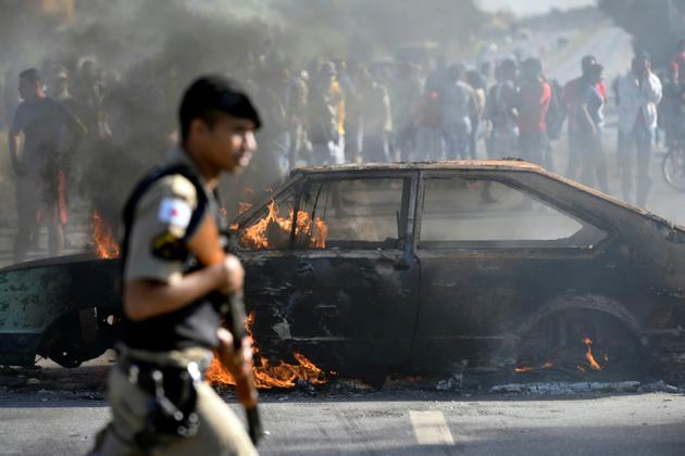 Un policier passe devant une voiture brûlée lors d'une manifestation contre la hausse du prix du diesel à Ribeirao das Neves au Brésil, le 25 mai 2018 [DOUGLAS MAGNO / AFP]