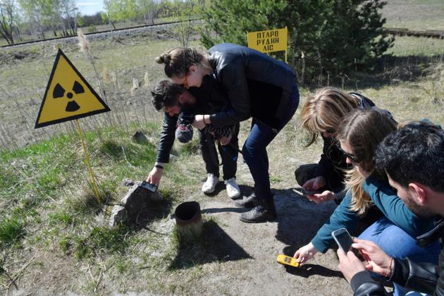 Des touristes mesurent le degré de radioactivité dans la "forêt rouge" devant le réacteur Numéro 4 de Tchernobyl, le 23 avril 2018 [Sergei SUPINSKY / AFP]