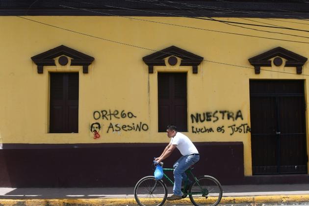 Un homme passe à bicyclette devant des inscriptions "Ortega assassin" et "Notre lutte est juste", dans la ville de Masaya, le 20 juin 2018 [MARVIN RECINOS / AFP]