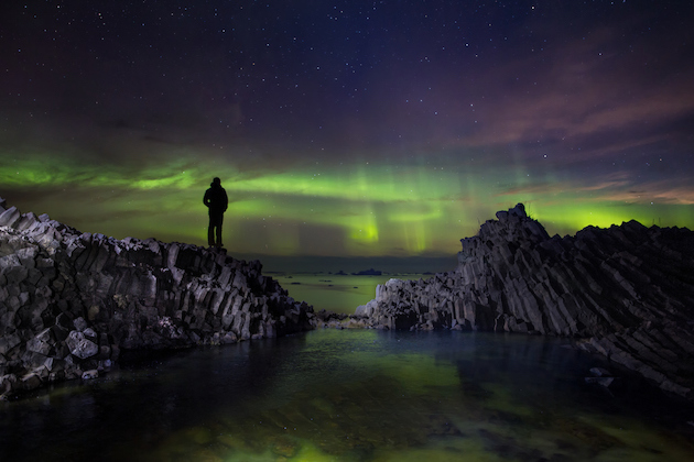 hiker_standing_on_volcanic_rooks_on_disko_island_in_north_greenland_photo_by_paul_zizka_-_visit_greenland_looking_at_northern_lights_dancing_over_the_ocean_5d5eaa89be557.jpg