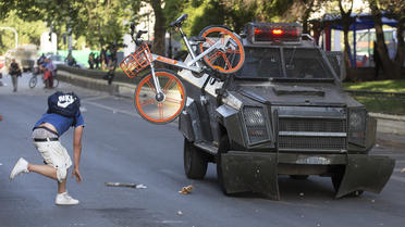 Un manifestant balance un vélo contre un véhicule de l'armée, le 18 octobre à Santiago.