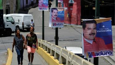 Des femmes marchent près d'une affiche de campagne du président vénézuélien Nicolas Maduro, dans les rues de Caracas, le 11 mai 2018 [Luis ROBAYO / AFP]