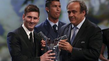 Lionel Messi reçoit des mains de Michel Platini, président de l'UEFA, le trophée de meilleur joueur UEFA de l'année devant Cristiano Ronaldo à la fin du tirage au sort de Ligue des Champions à Monaco le 27 août 2015 [VALERY HACHE / AFP]