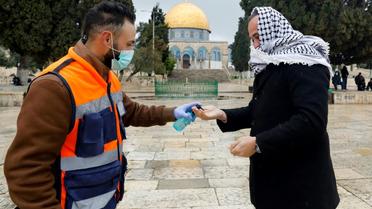 Un volontaire propose du gel hydroalcoolique à un palestinien en route pour la prière du vendredi, devant la mosquée Al-Aqsa à Jérusalem, le 20 mars 2020 [AHMAD GHARABLI / AFP]