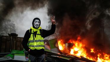 Un manifestant portant un gilet jaune et un masque près d'une barricade en feu, à Paris le 1er décembre 2018 [Abdulmonam EASSA / AFP]