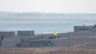 Photo prise depuis le côté turc de la frontière turco-syrienne, montrant un drapeau des Unités de protection du peuple (YPG) flottant au-dessus d'un bâtiment près de la ville syrienne de Tal Abyad, le 8 octobre 2019 [BULENT KILIC / AFP]
