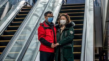 Un couple portant des masques de protection, devant un centre commercial désert, à Pékin le 22 février 2020 [NICOLAS ASFOURI / AFP]