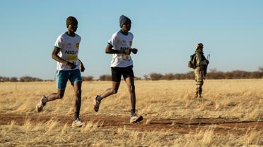 Deux marathoniens passent devant un soldat lors du premier marathon jamais organisé au Niger, le 29 décembre à Agadez. [Nora Schweitzer / AFP]