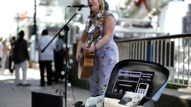 La chanteuse de rue Charlotte Campbell utilise un lecteur de carte bancaire sans contact pour récolter des dons, au pied du London Eye (grande roue) à Londres le 1er septembre 2018 [Daniel LEAL-OLIVAS / AFP]