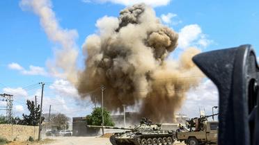 Photo prise le 12 avril 2019 montrant une colonne de fumée s'élever derrière des chars des forces loyales au Gouvernement d'union nationale (GNA) à Wadi Rabi, à quelque 30 km au sud de la capitale libyenne [Mahmud TURKIA / AFP]