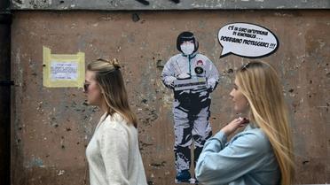 Deux femmes passent devant un message mural où il est écrit: "Il y a une épidémie d'ignorance dans l'air, nous devons nous protéger", par l'artiste Laika, près du quartier chinois de Rome, le 4 février 2020 [Filippo MONTEFORTE / AFP/Archives]