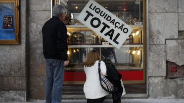 Des passants devant la vitrine d'un magasin liquidant son stock à Lisbonne, le 16 décembre 2013 [Pedro Nunes / AFP]