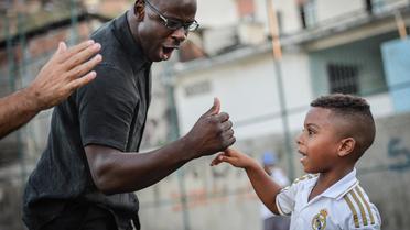 Le footballeur français Lilian Thuram  avec un enfant de 5 ans lors d'une visite dans une favela de Rio de Janeiro le 15 mars 2014 à Rio de Janeiro [Yasuyoshi Chiba / AFP]