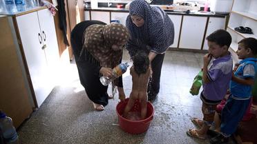Feriel al-Zaaneen lave sa fille Sama dans une bassine à l'aide de bouteilles d'eau dans une école de l'ONU à Jabalia le 16 août 2014 [Roberto Schmidt / AFP]