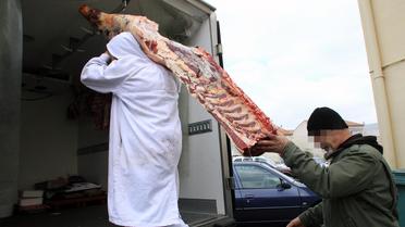 Un employé réquisitionné transporte un quartier de viande sous la surveillance d'un policier le 16 décembre 2013 à Narbonne  [Raymond Roig / AFP]