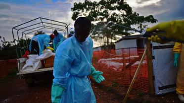 Un membre des services publics de fossoyeurs en Sierra Leone est aspergé de désinfectant tandis que des collègues chargent un camion des corps de victimes du virus Ebola, à Kailahun, le 14 août 2014 [Carl de Souza / AFP]