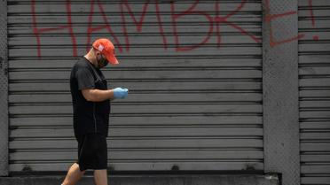 Un homme, protégé par un masque contre le coronavirus, passe devant un rideau de fer où est écrit "Faim", à Caracas, le 14 mai 2020 [Federico PARRA / AFP]