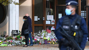 Des gens regardent des fleurs déposées devant le lycée du Bois d'Aulne en hommage au professeur d'histoire assassiné Samuel Paty, le 19 octobre 2020, à Conflans-Sainte-Honorine, au nord-ouest de Paris. 