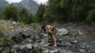 Un homme habillé comme un homme de Neanderthal se lave dans une rivière des Alpes italiennes [MARCO BERTORELLO / AFP/Archives]