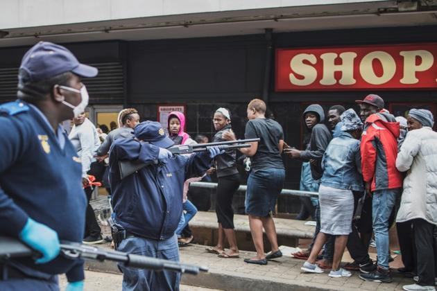 Un policier pointe son arme sur des clients d'un supermarché pour leur faire respecter la distanciation sociale, à Johannesburg, le 28 mars 2020 [MARCO LONGARI / AFP]
