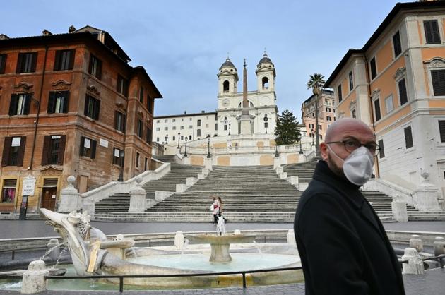 Un homme qui porte un masque contre le coronavirus marche près de la Place d'Espagne déserte à Rome le 12 mars 2020 [Alberto PIZZOLI / AFP]