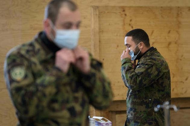 Deux militaires de l'armée suisse enfilent un masque de protection lors d'une formation à Bière (ouest) le 22 mars 2020 [Fabrice COFFRINI / AFP]