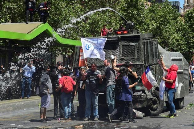 Des manifestants se tiennent devant un canon à eau de la police, à Santiago le 23 octobre 2019 [Martin BERNETTI                      / AFP]