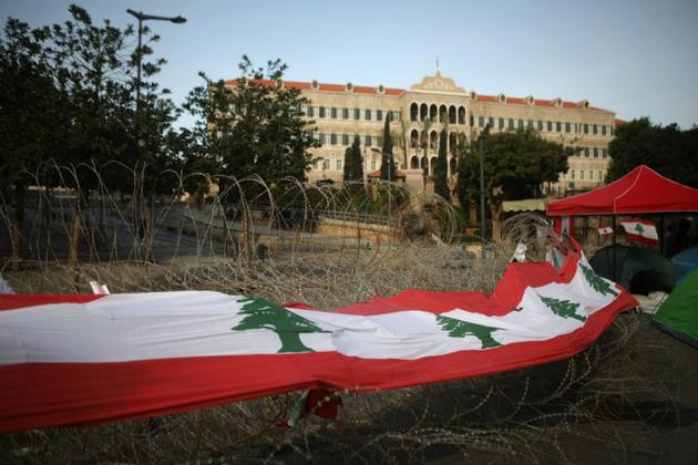 Un large drapeau libanais placé sur les barbelés devant le siège du gouvernement à Beyrouth, le 26 octobre 2019  [Patrick BAZ / AFP]