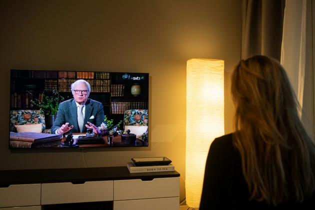 Une femme regarde l'allocution du roi de Suède Carl XVI Gustaf à la télévision, le 5 avril 2020 à Sundbyberg près de Stockholm [Jonathan NACKSTRAND / AFP]