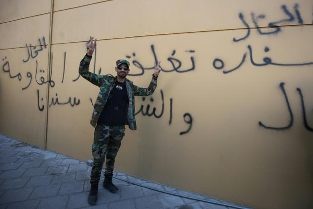 Un membre du Hachd al-Chaabi, coalition de paramilitaires dominée par des factions pro-Iran, fait le V de la victoire devant un graffitti en arabe sur le mur de l'ambassade des Etats-Unis à Bagdad, qui affirme : 