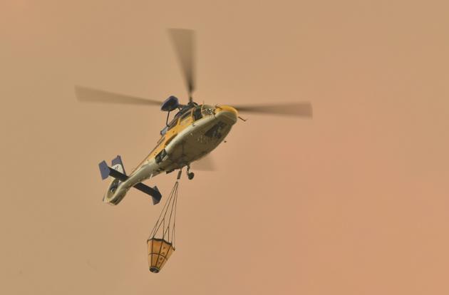 Un hélicoptère va larguer une charge d'eau sur un feu de forêt à Bargo, le 21 décembre 2019 en Australie [PETER PARKS / AFP]
