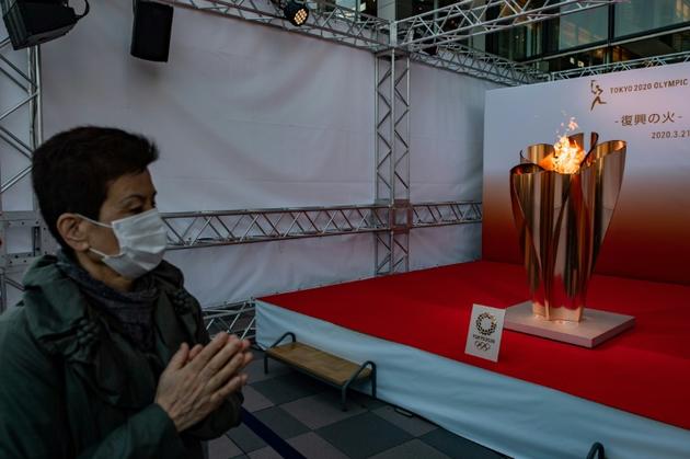 La flamme olympique, sous le regard d'un Japonais portant un masque, lors de son passage à Sendai, au nord du Japon, le 21 mars 2020 [Philip FONG / AFP]