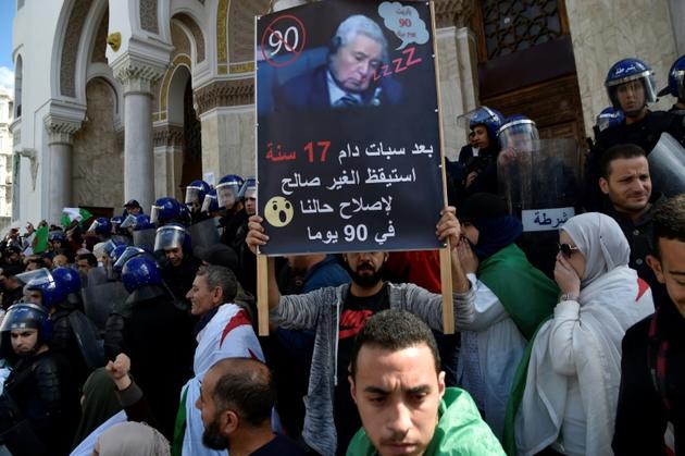 Lors d'une manifestation le 10 avril 2019 à Alger, un manifestant brandit une pancarte où figure Abdelkader Bensalah et est écrit en arabe: "Après 17 ans de coma, le malade s'est réveillé pour régler notre situation en 90 jours" [RYAD KRAMDI                         / AFP]