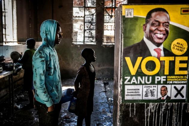 Dans une banlieue d'Harare, le 27 juillet 2018, un jeune homme attend devant une affiche représentant le président zimbabwéen Emmerson Mnangagwa, patron de la Zanu-PF, le parti au pouvoir  [Luis TATO / AFP]