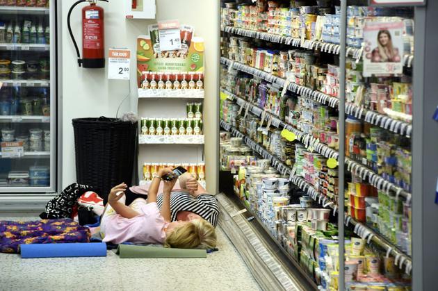 Des femmes prennent un selfie le 4 août 2018 près des étagères réfrigérées d'un supermarché à Helsinki, qui a autorisé ses clients à dormir dans ses locaux pour se protéger de la chaleur, durant le week-end. [Heikki Saukkomaa / Lehtikuva/AFP]