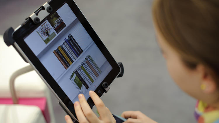 Une femme choisit un livre dans une bibliothèque sur une tablette numérique [Robert Michael / AFP/Archives]