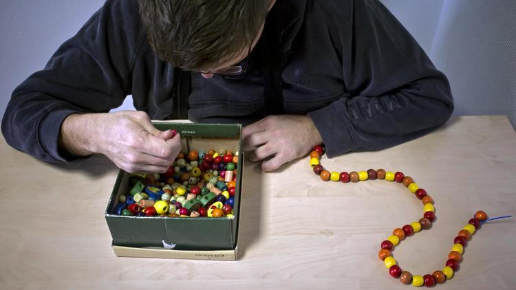 Une personne autiste réalise un collier de perles avec l'aide du personnel d'un centre médical français [Jean-Philippe Ksiazek / AFP/Archives]
