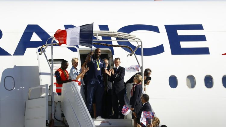 Le double médaillé d'or olympique en judo Teddy Riner, drapeau à la main, à sa descente de l'avion de retour des Jeux de Rio sur le tarmac de l'aéroport Charles de Gaulle à Roissy le 23 août 2016 [PATRICK KOVARIK / AFP]