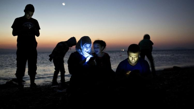 Des migrants consultent leur téléphone portable laors qu'ils viennent d'accoster avec leur embarcation de fortune sur une plage de l'île grecque de Kos, le 12 août 2015 [Angelos Tzortzinis / AFP/Archives]