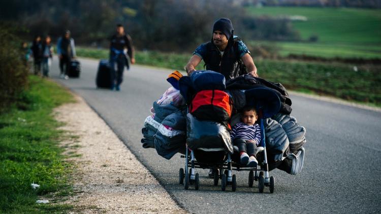 Un homme transporte dans une poussette son fils et des affaires personnelles sur une route près de la frontière entre la Grèce et la Macédoine, le 8 mars 2016 [DIMITAR DILKOFF / AFP]