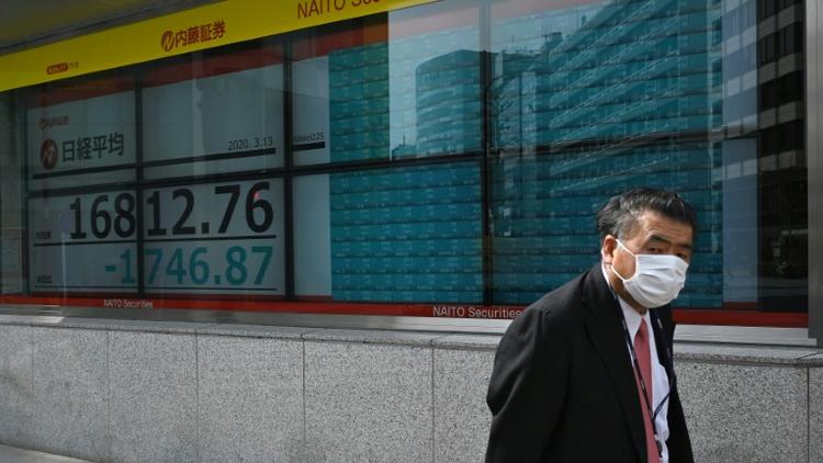 Un homme masqué passe devant un écran de la Bourse de Tokyo en chute, le 13 mars 2020 [Philip FONG / AFP]