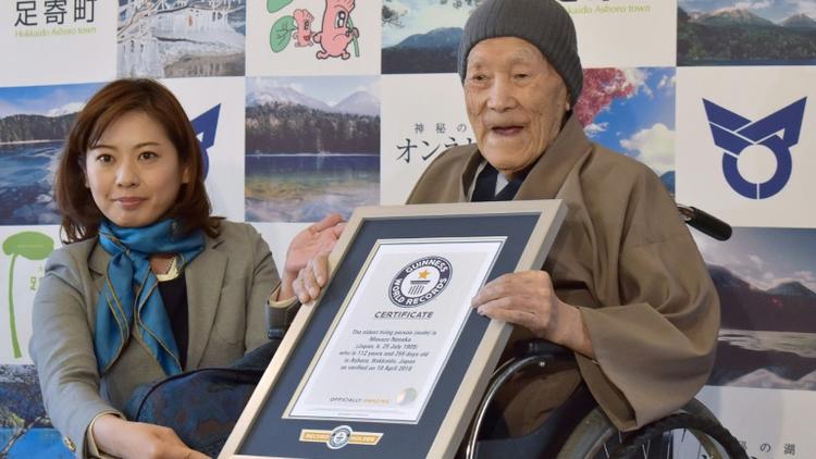 Masazo Nonaka (D), alors âgé de 112 ans, sourit en recevant son certificat d'homme le plus âgé du monde des mains d'Erika Ogawa (G), vice-présidente au Japon du Guinness des records, à Ashoro dans la préfecture d'Hokkaido le 10 avril 2018 [JIJI PRESS / JIJI PRESS/AFP/Archives]