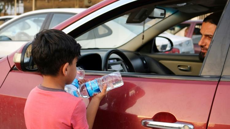 Un garçon irakien essaye de vendre des bouteilles d'eau dans une rue de Mossoul, où des enfants orphelins errent pour mendier ou vendre des objets futiles pour survivre, un an après la reprise par l'armée irakienne de la ville aux jihadistes, le 7 juillet 2018 [Waleed AL-KHALID / AFP Photo]