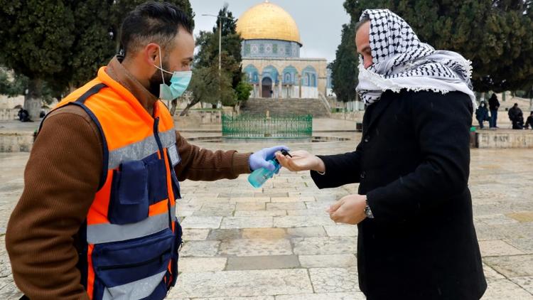 Un volontaire propose du gel hydroalcoolique à un palestinien en route pour la prière du vendredi, devant la mosquée Al-Aqsa à Jérusalem, le 20 mars 2020 [AHMAD GHARABLI / AFP]