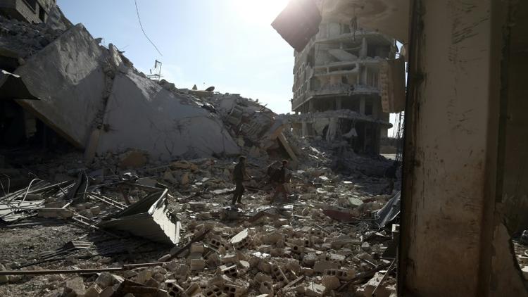 Des Syriens au milieu des destructions dans la localité de Saqba, dans l'enclave rebelle de la Ghouta orientale, bombardée par le régime syrien, le 9 mars 2018  [ABDULMONAM EASSA / AFP]